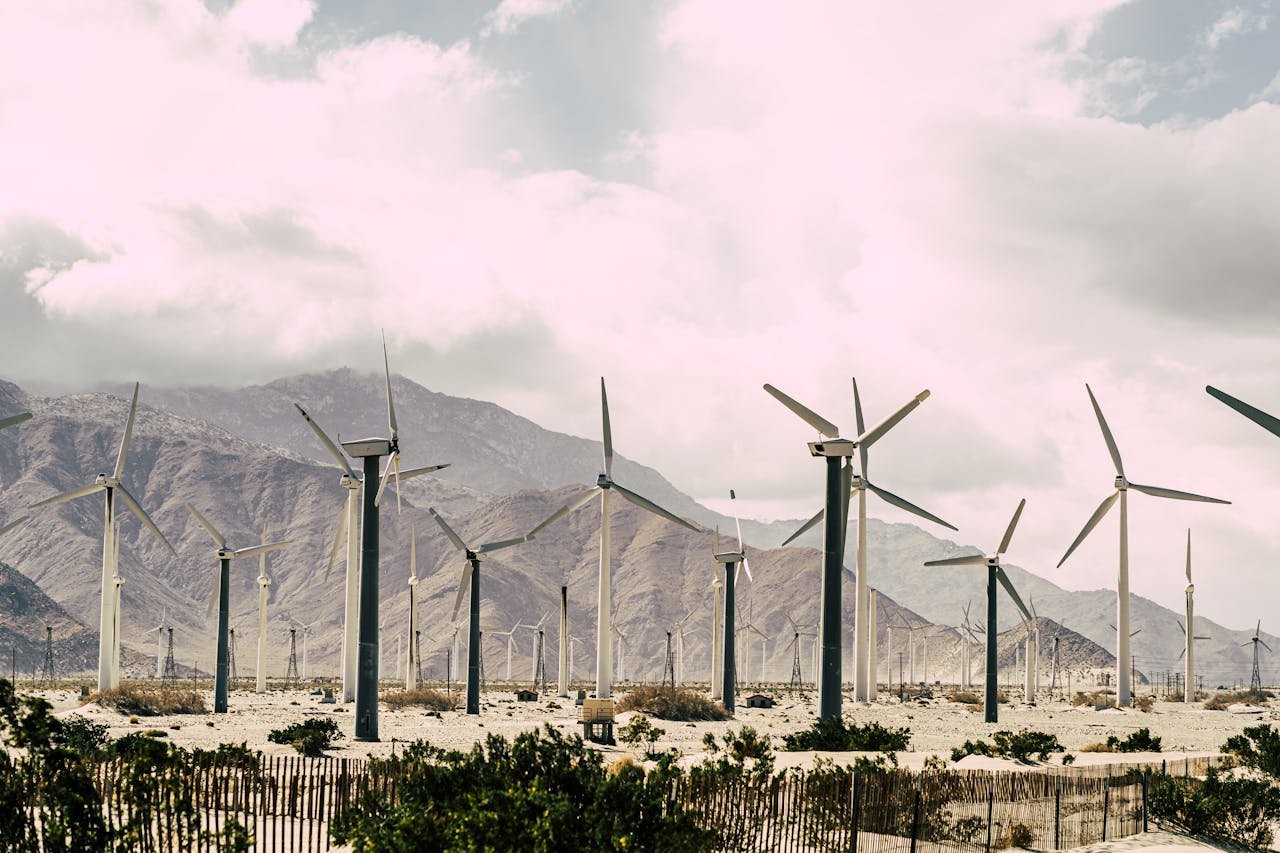 Capture of a wind farm set against a dramatic mountain backdrop under a cloudy sky.